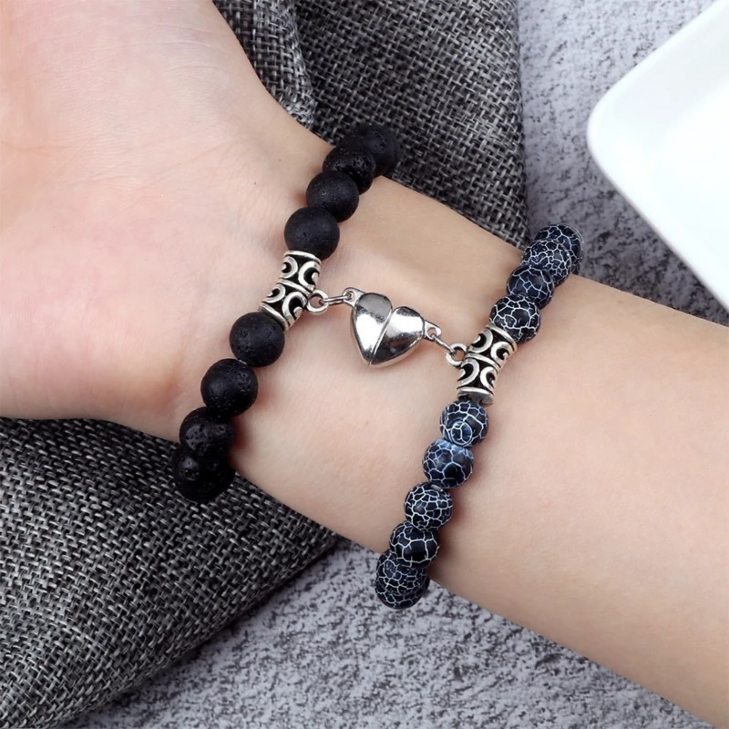 two couple's matching beaded bracelet attached together with magnetic heart on a person's wrist.